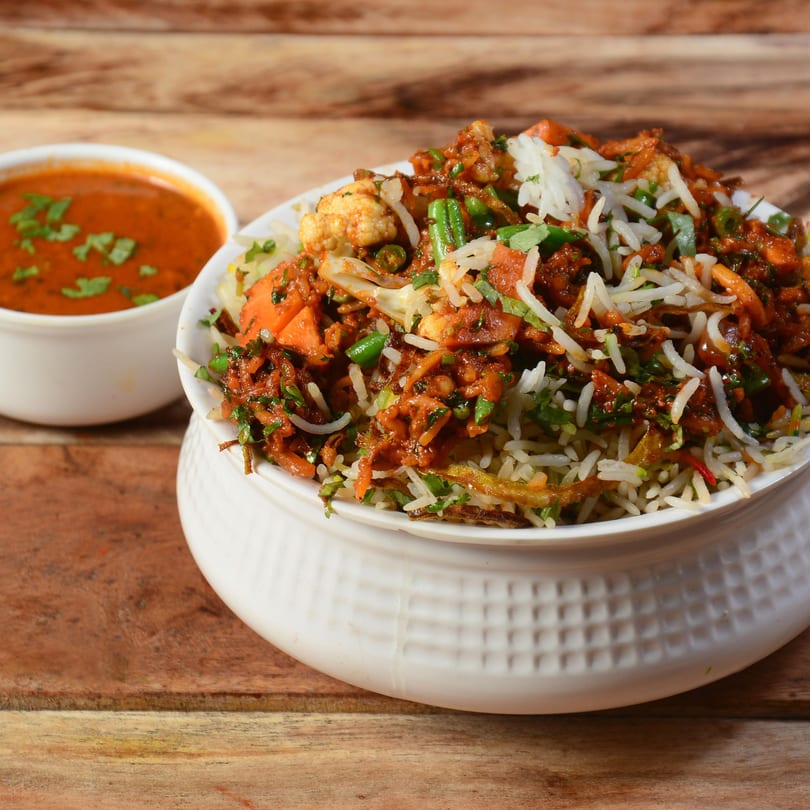 Vegetable Biryani, an Indian rice dish, in a white bowl with a side of curry.